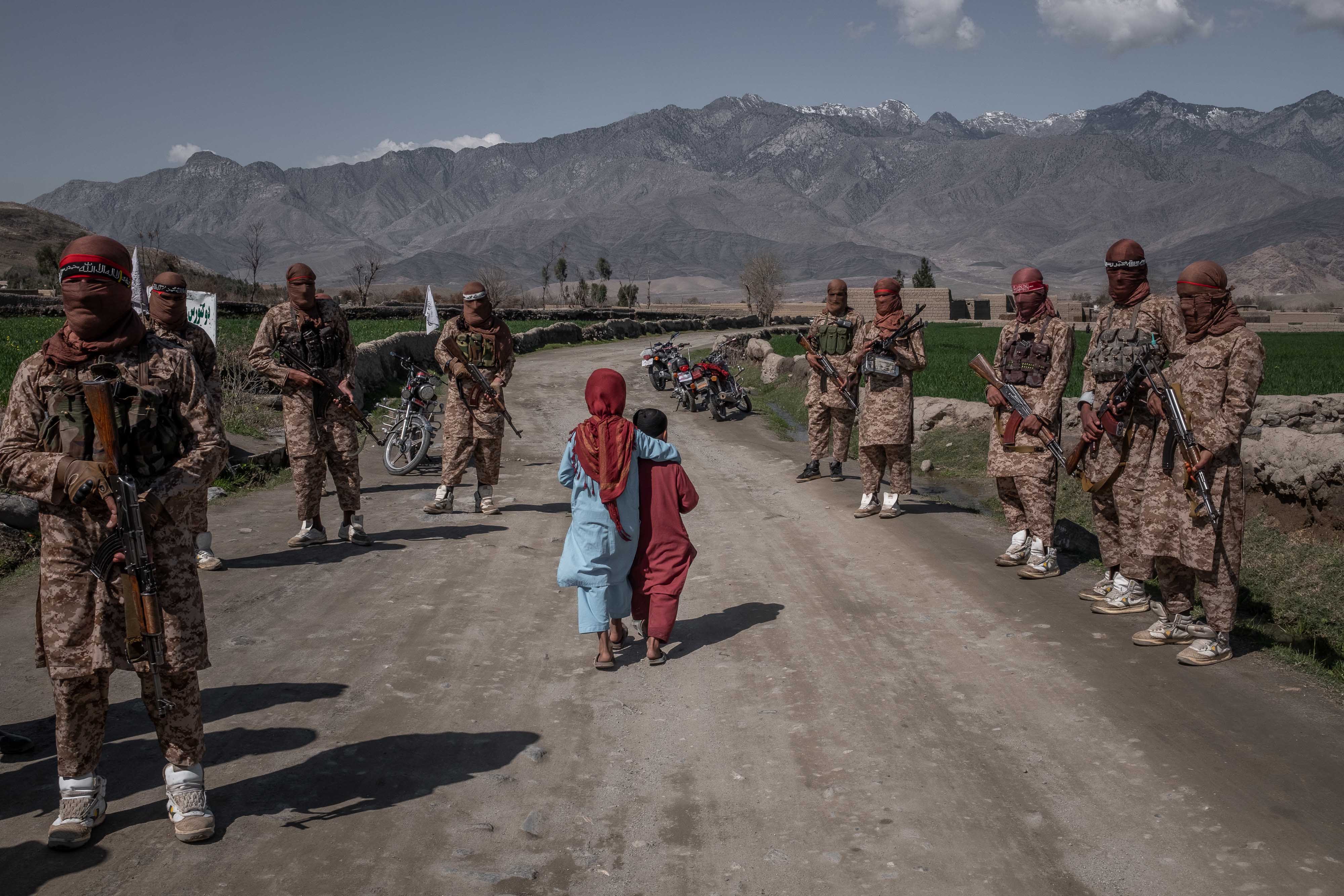 Two children walk by armed soldiers in the countryside