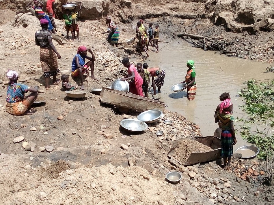 A group of adults and children with pans next to a muddy river