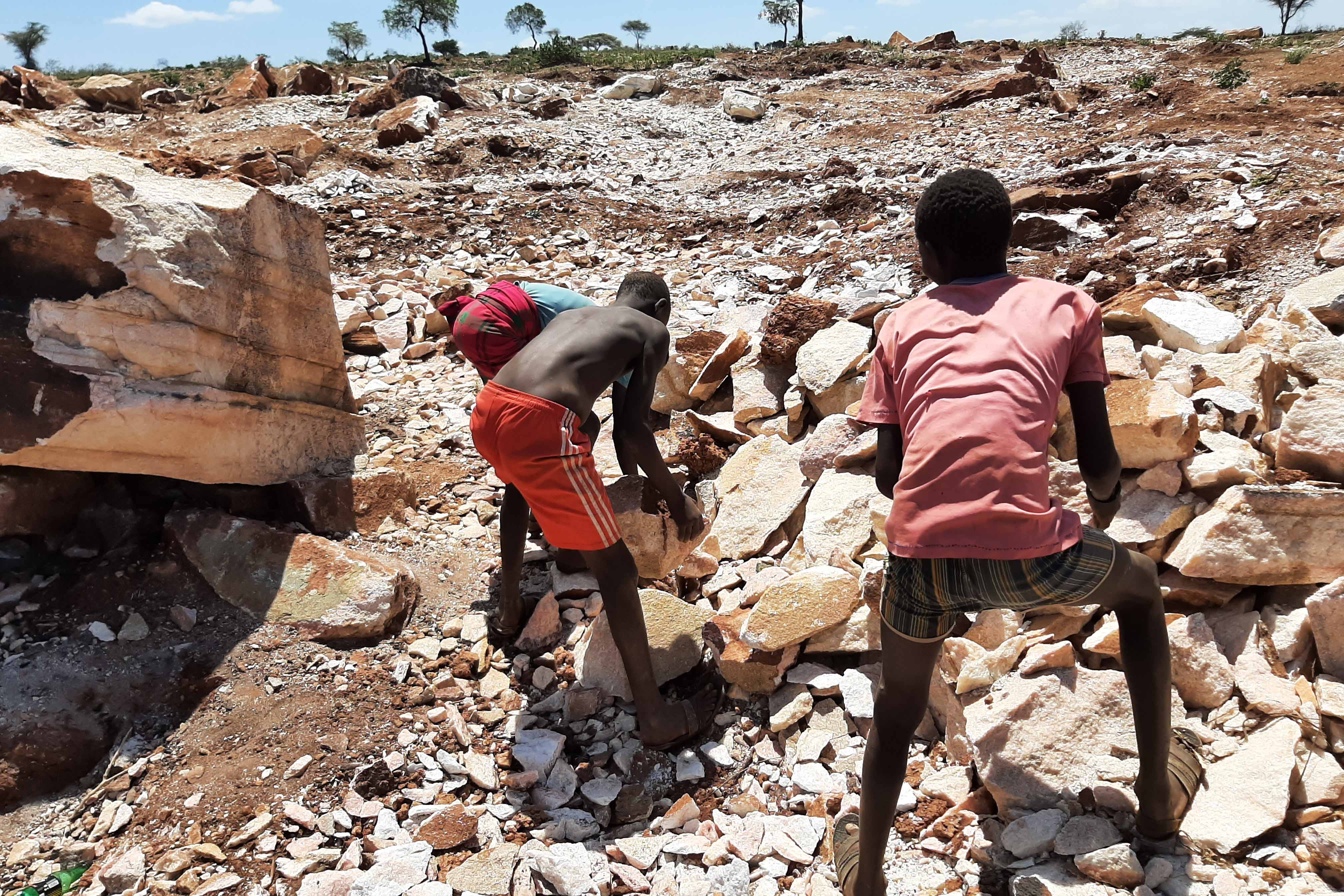 Two boys pick up large rocks at a quarry 