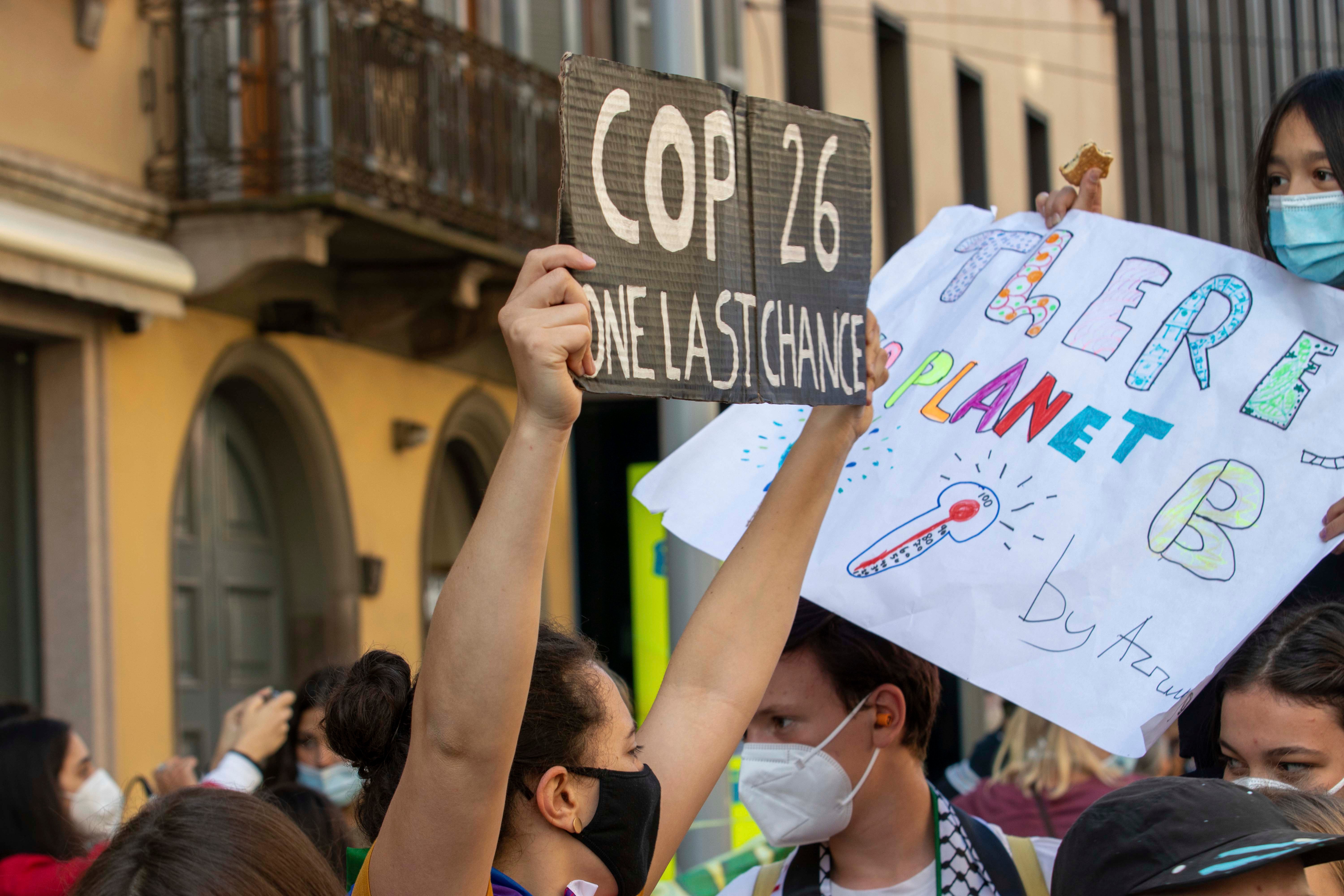 A masked person holds a sign that says "COP26: One Last Chance"
