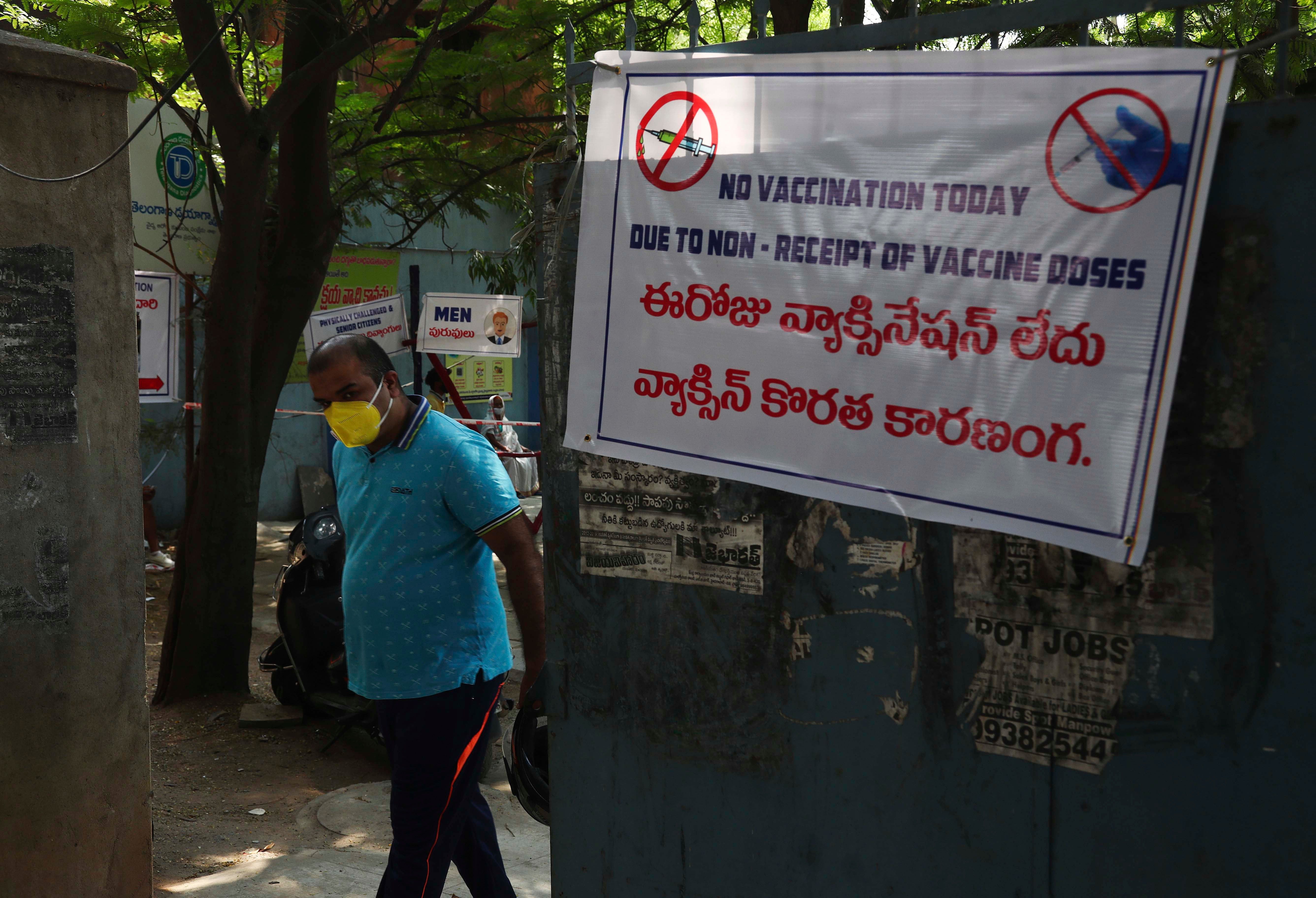 A man in a face mask stands next to a sign that says "No vaccination today" in English and Hindi