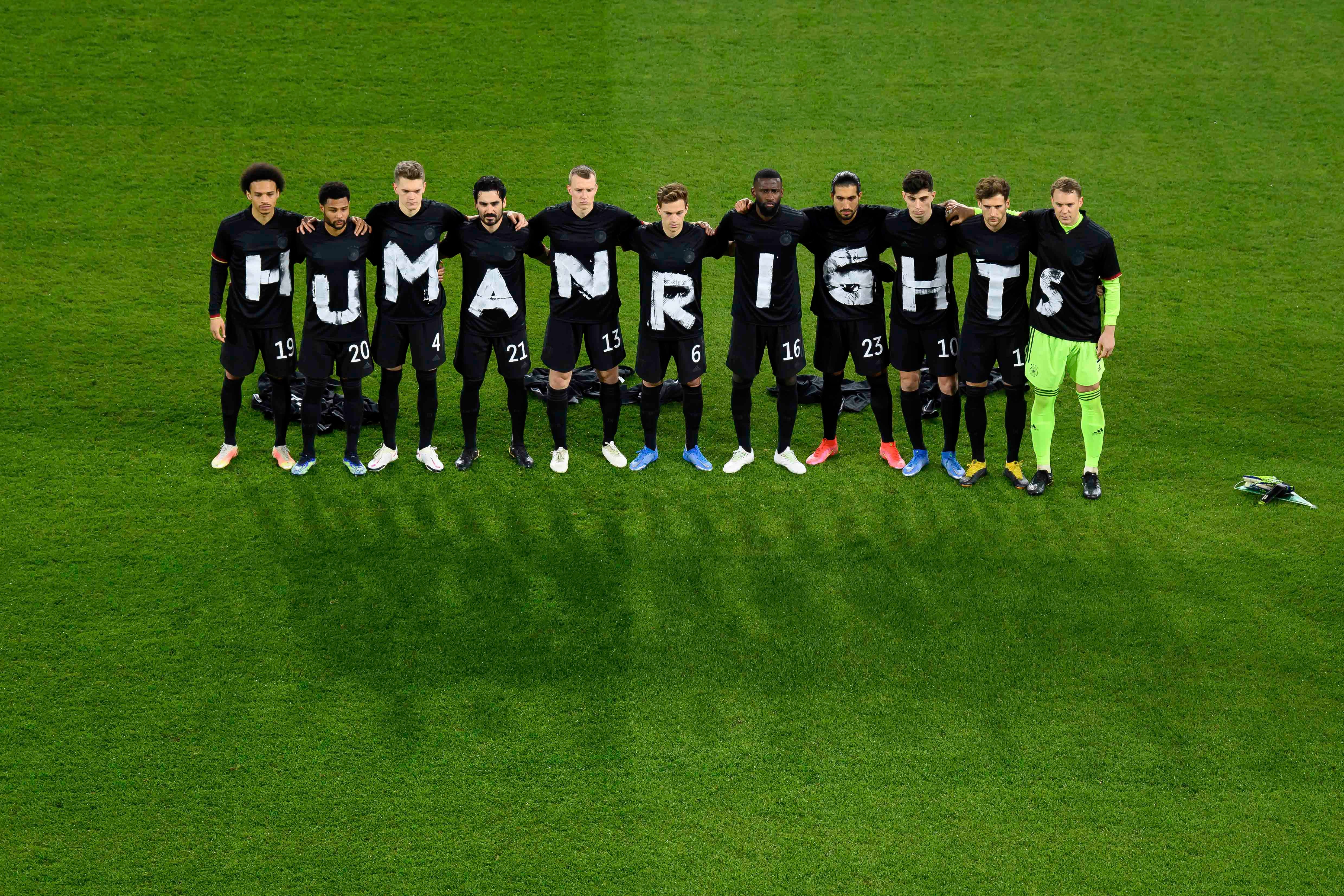 Soccer players stand in a line wearing shirts that spell out "HUMAN RIGHTS"