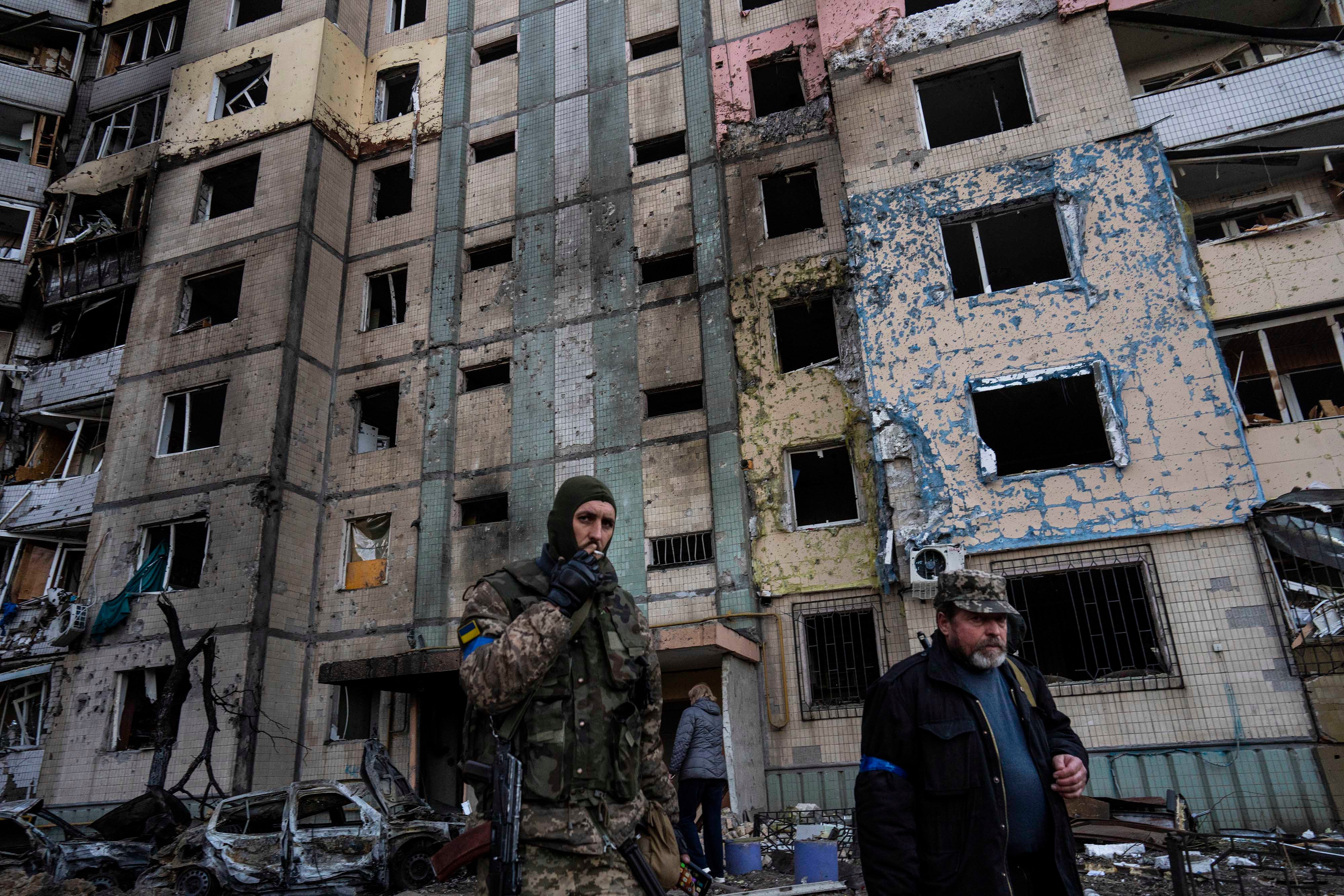 A soldier smokes a cigarette while walking next to a destroyed building