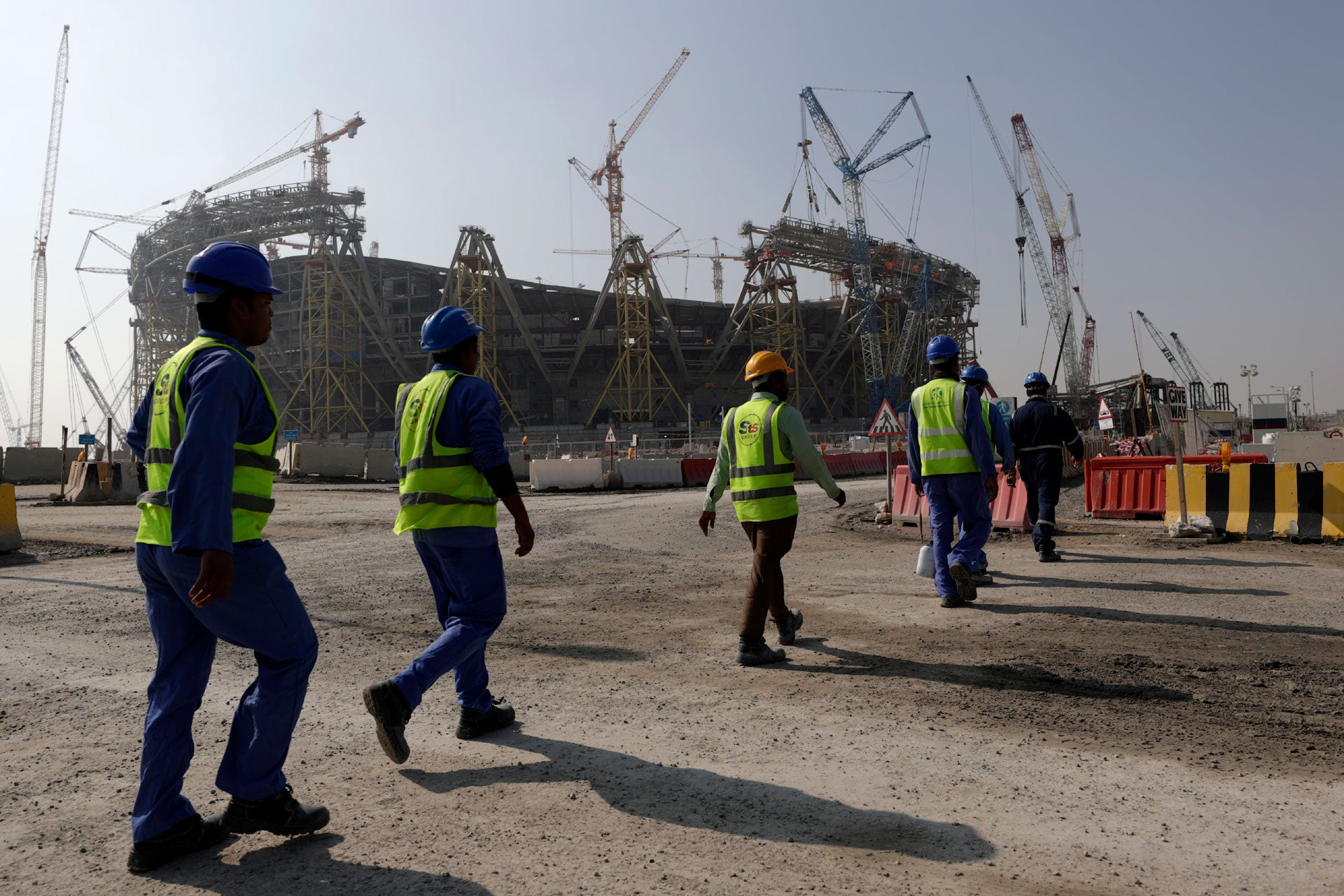 Workers walk toward a sports stadium under construction