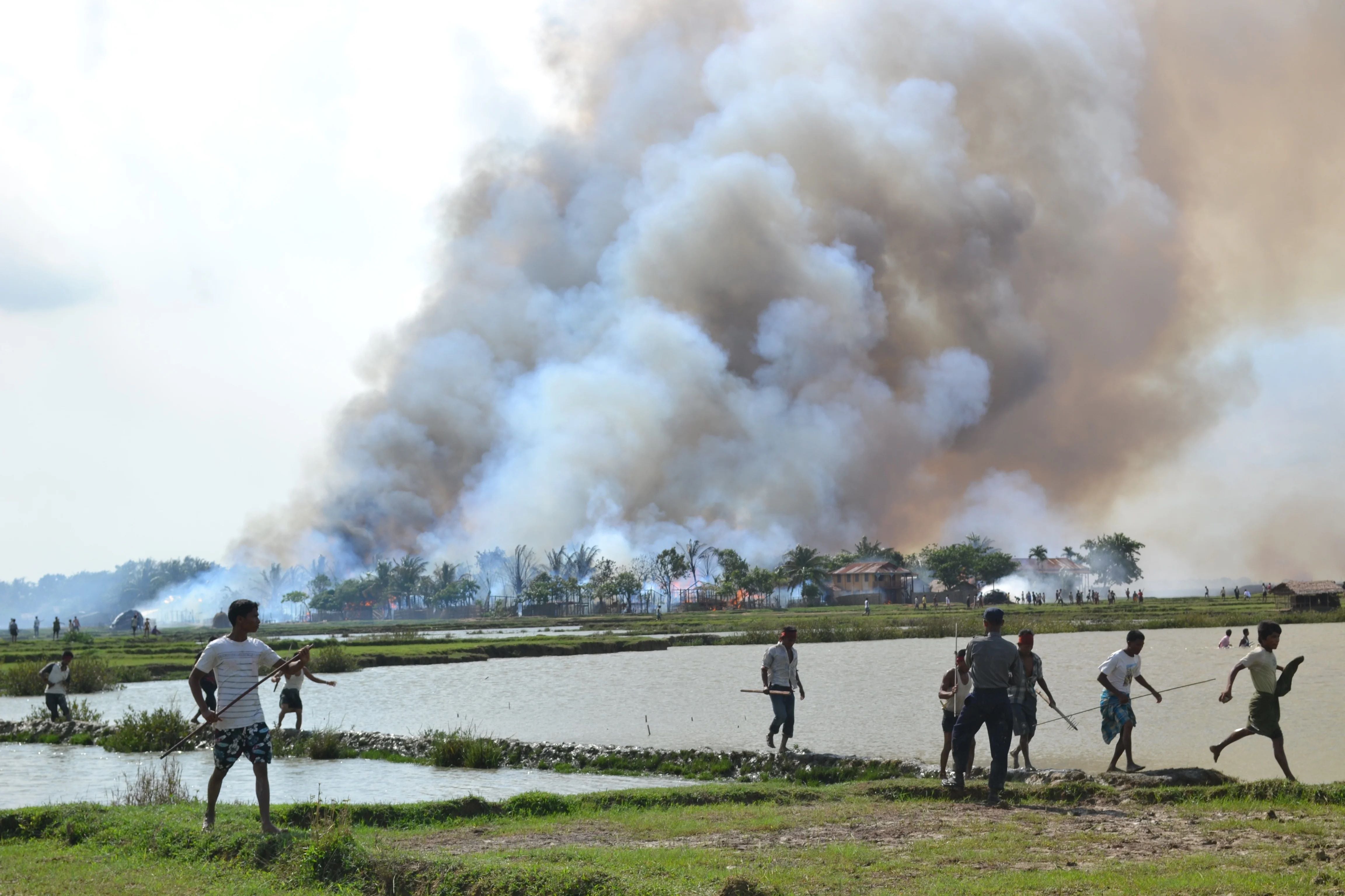 Ethnic Rakhine with weapons walk away from a village in flames while a soldier stands by, June 2012.