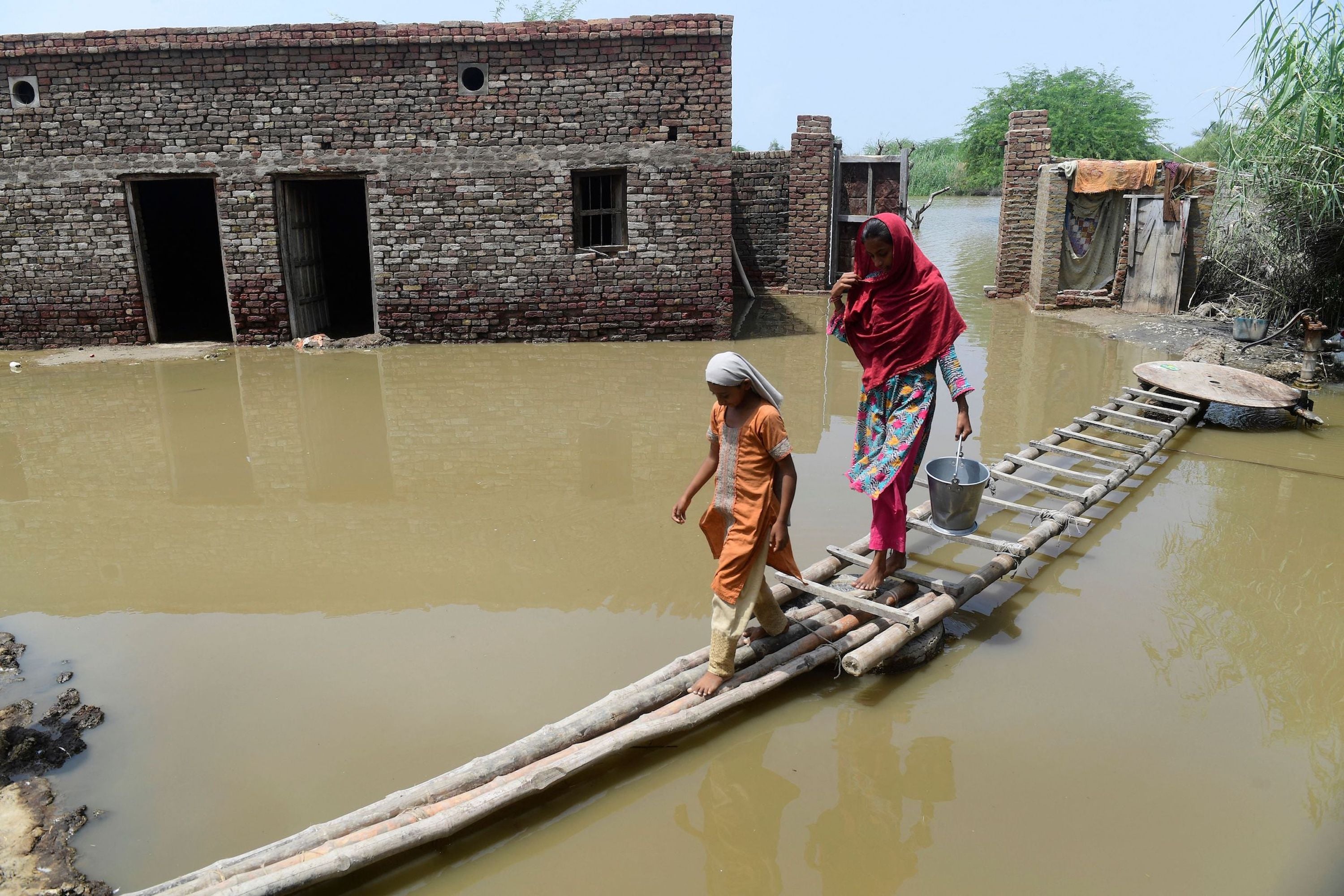 A woman and girl walk on a temporary bamboo path near their flooded house in Shikarpur, Pakistan.