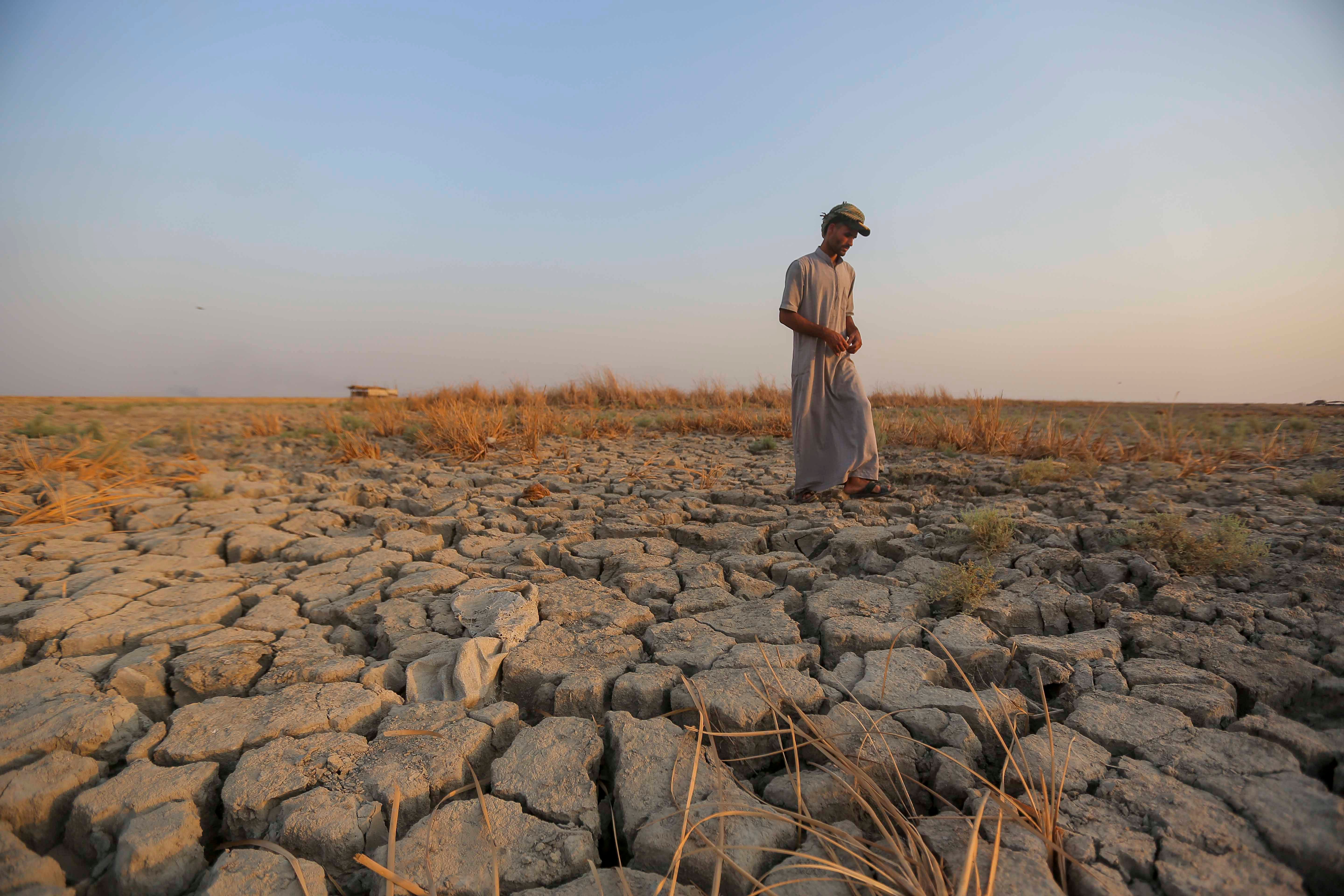 A fisherman walks across a dried patch of land in the marshes of southern Iraq in Dhi Qar province, September 2, 2022. Iraq's marshlands are rapidly receding due to drought, domestic water mismanagement, and diversion from neighboring countries.