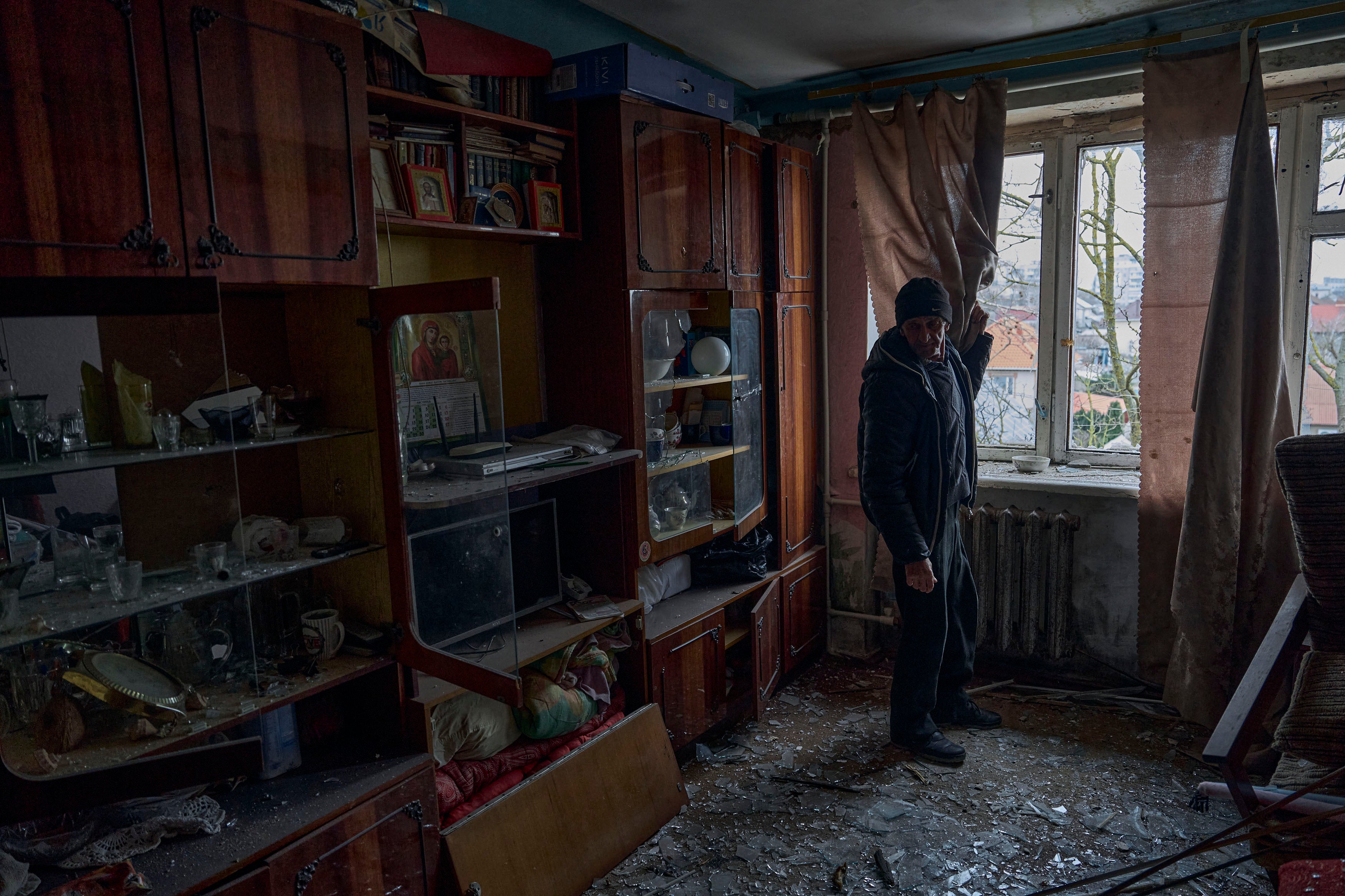 A man looks at shards of glass on his apartment floor 