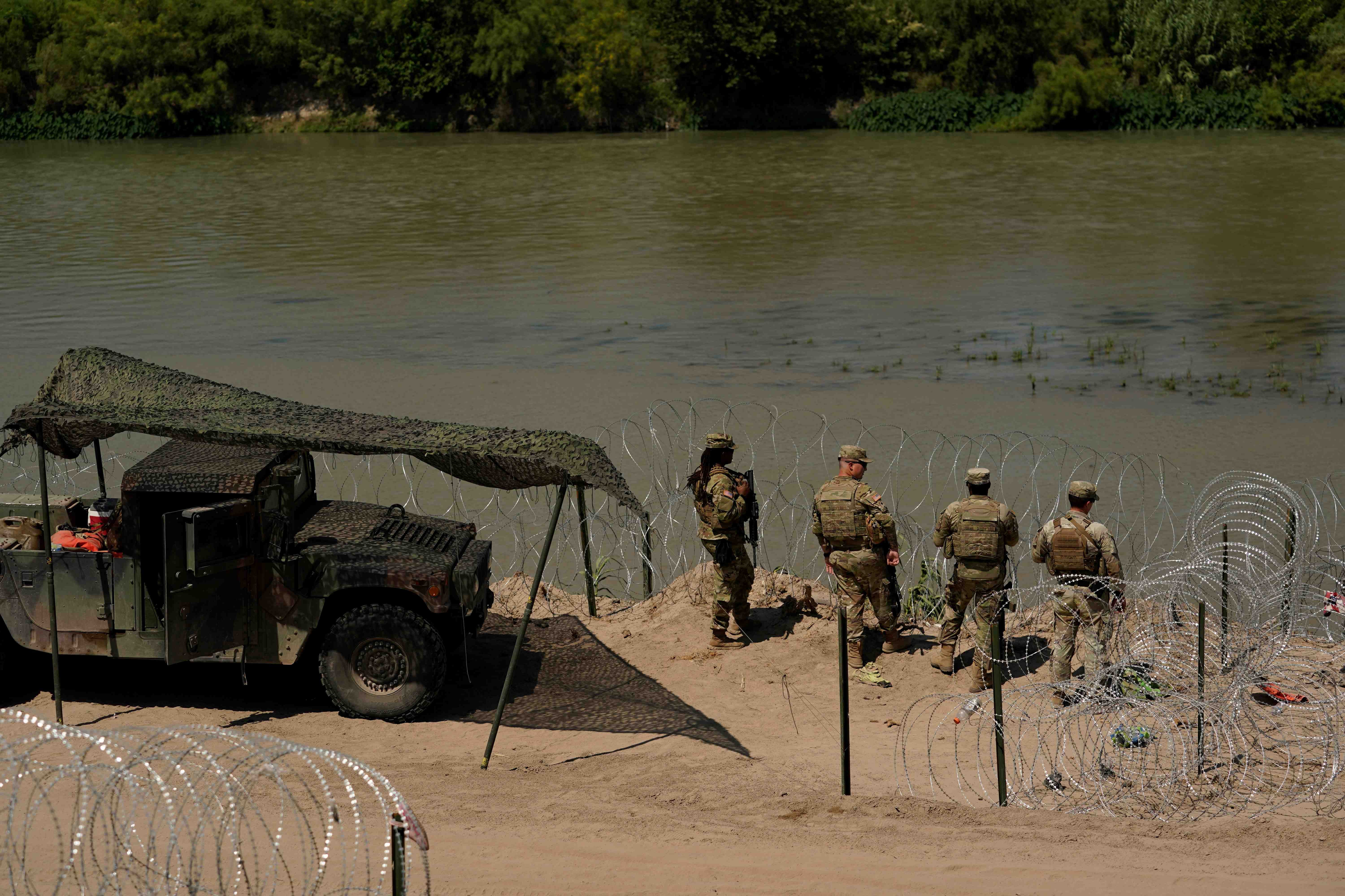 Guardsmen stand by a river lined with razorwire