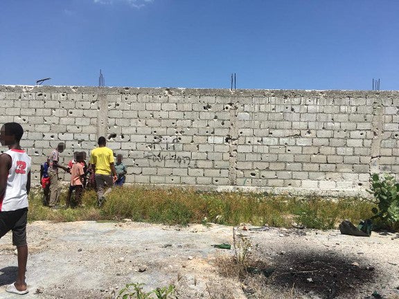 People stand in front of a wall with bullet holes