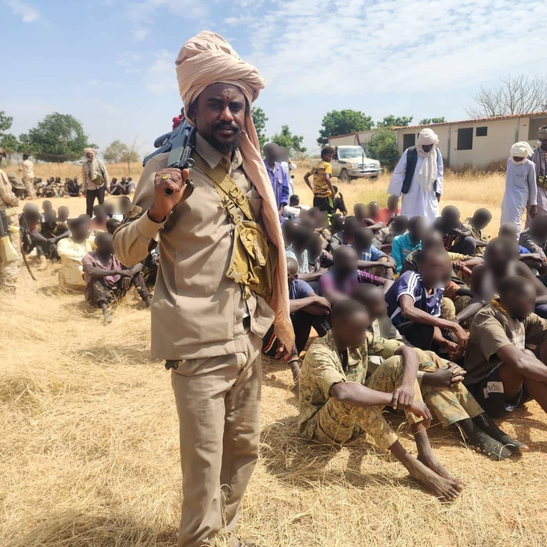 Fighters stand over a group of men seated on the ground