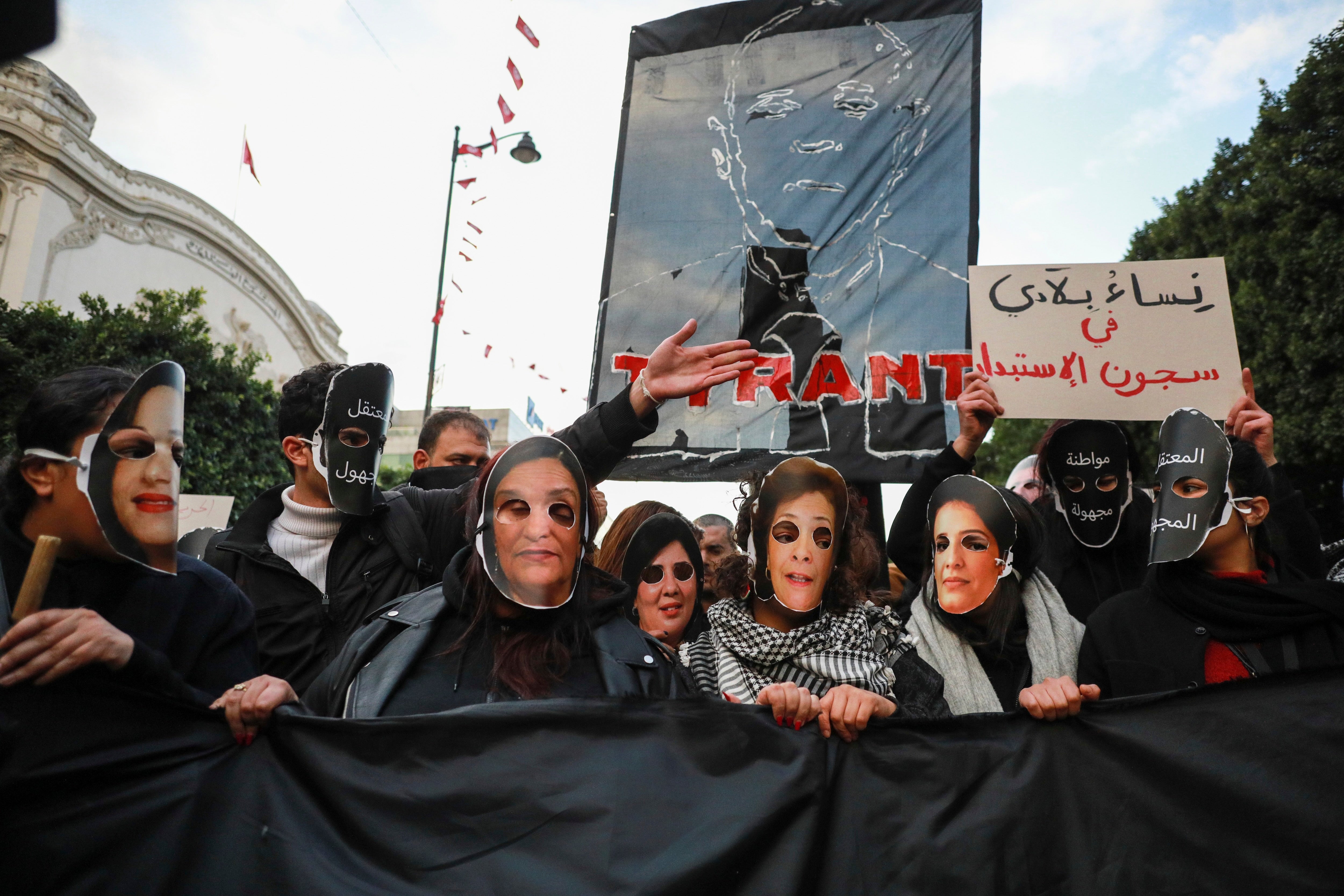 Demonstrators hold up a banner bearing the effigy of Tunisian President Kais Saied that reads ''Tyrant,'' while others wear masks representing Tunisian women jailed or detained by the authorities including Bensedrine , during a protest in Tunis, January 14, 2025. 
