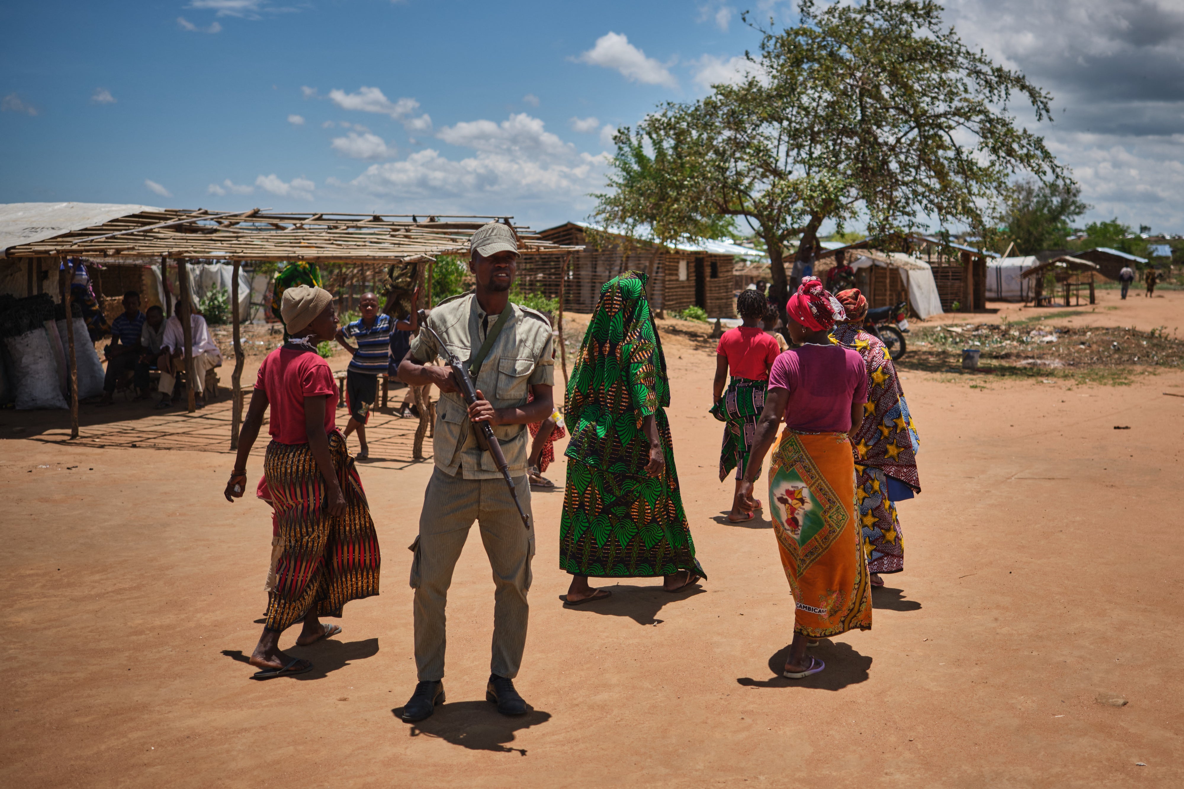 A police officer patrols in front of women in a shelter for internally displaced people