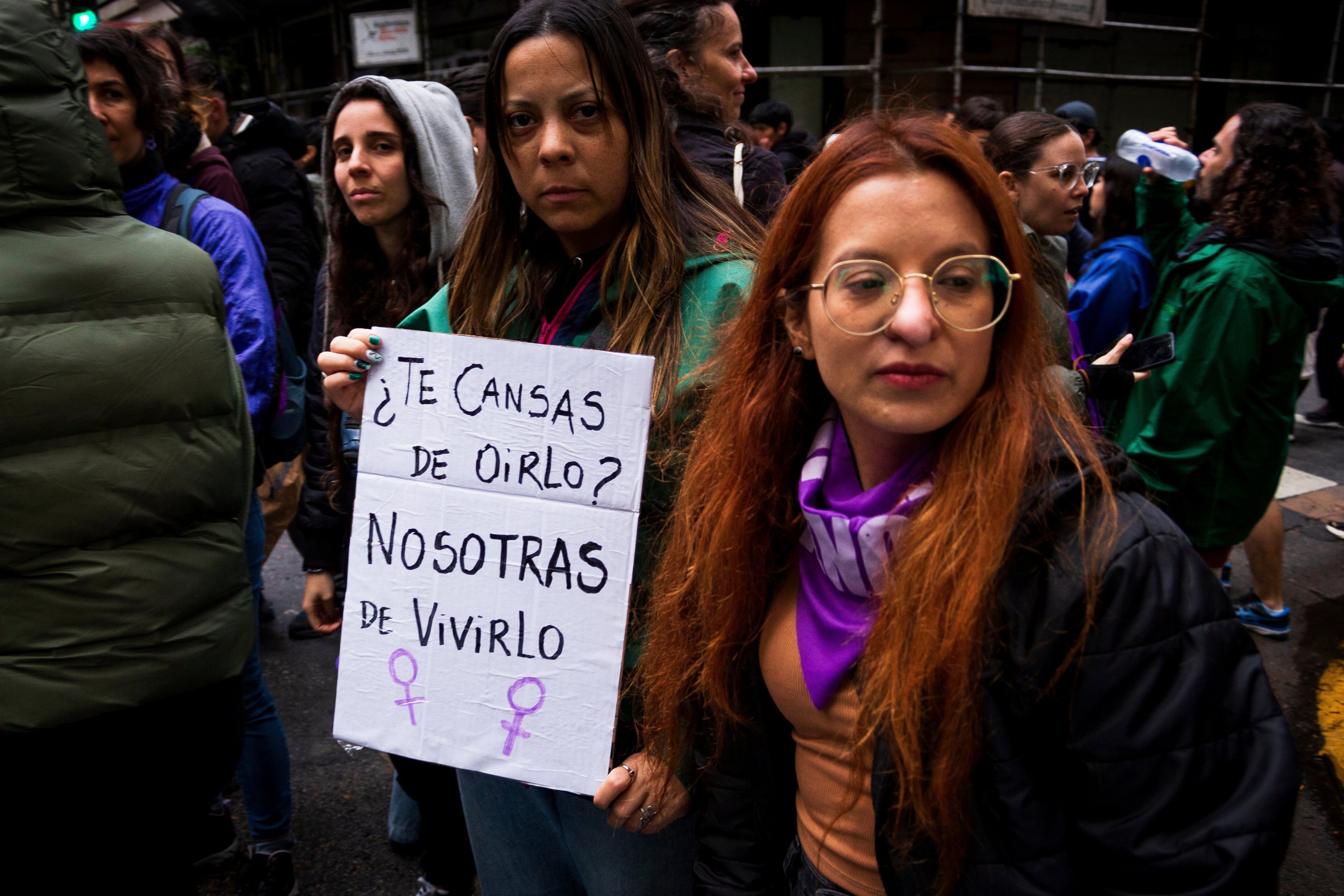 Two women hold a sign that reads “You’re tired of hearing it? We're tired of living it.”