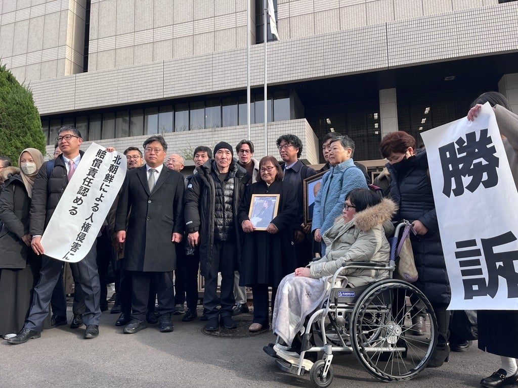 Plaintiffs holding flags declaring the verdict in front of the Tokyo district court main gate, January 26, 2026. 