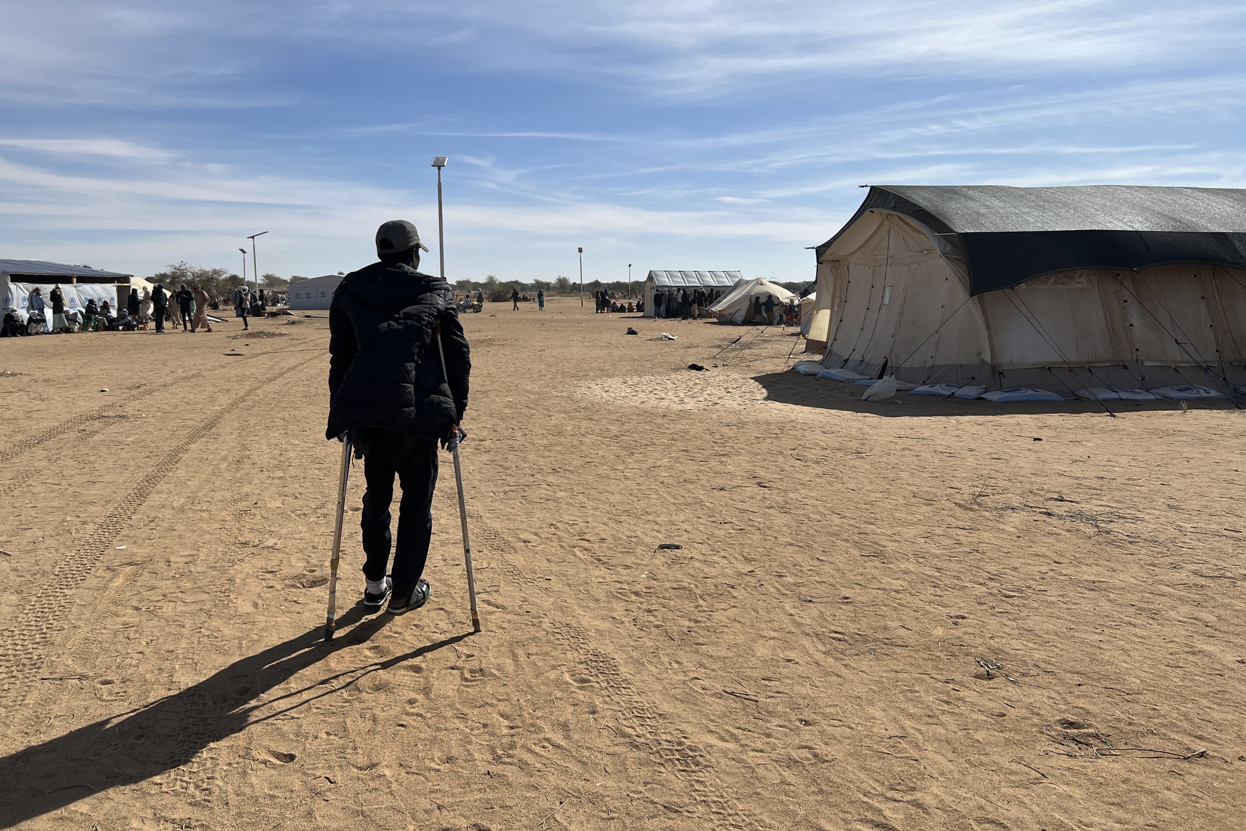 A man stands on crutches in a refugee camp