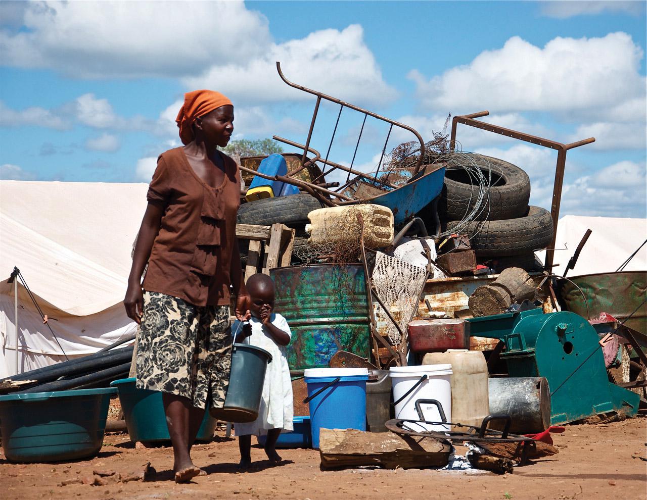  A woman stands in front of a pile of her household property at Chingwizi transit camp, which the government forcibly shut down in August 2014. Hundreds of families lost their property left in the open during their relocation to the camp. March 2014.