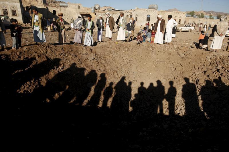 People stand around a crater caused by a Saudi-led air strike on the outskirts of Yemen's capital Sanaa, December 29, 2015. 
