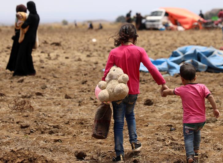 An Internally displaced girl from Daraa province carries a stuffed toy and holds the hand of child near the Israeli-occupied Golan Heights in Quneitra, Syria June 29, 2018. © 2018 Reuters/Alaa Al-Faqir
