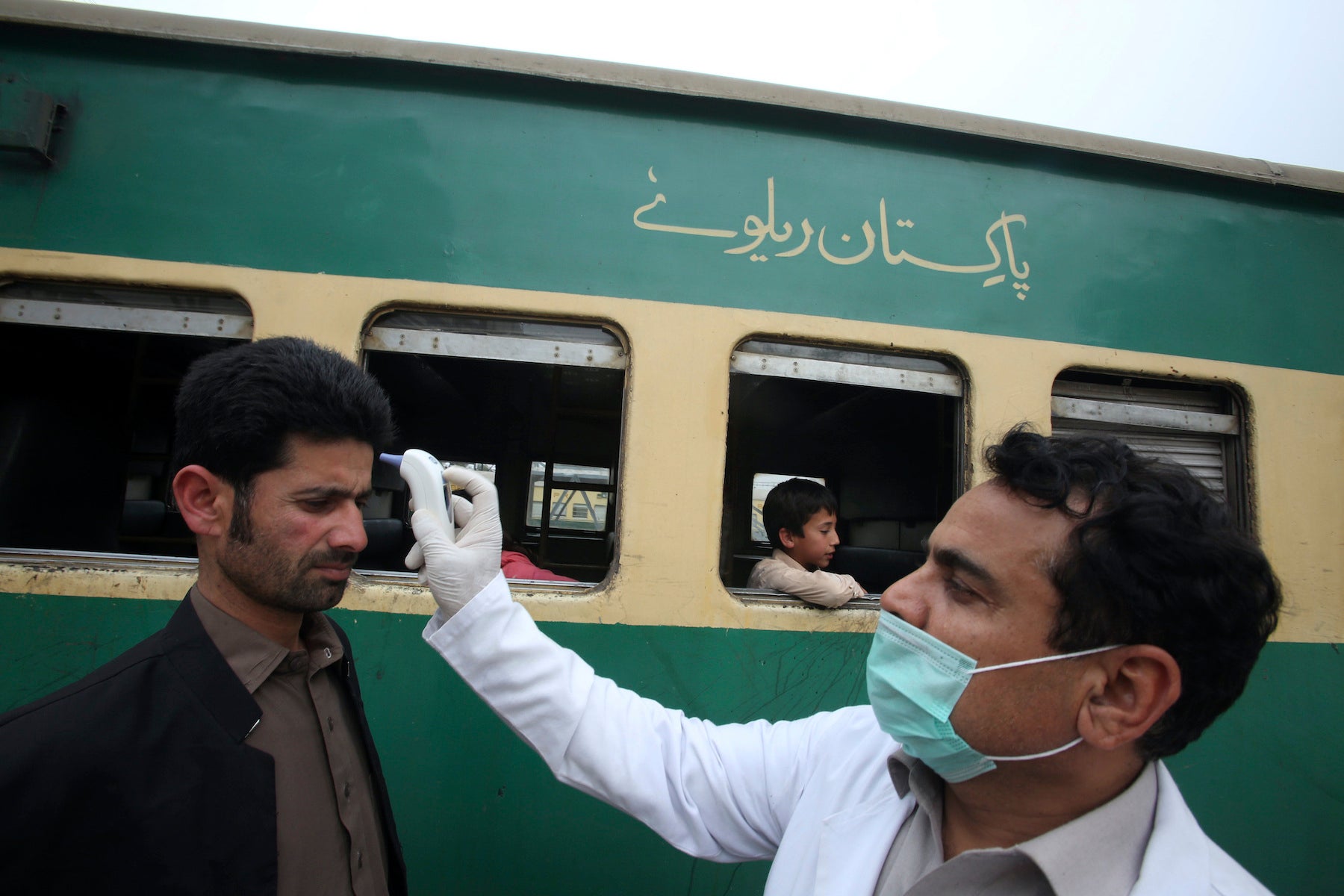 A volunteer checks the temperature of passengers arriving at a railway station in Peshawar, Pakistan, March 17, 2020.