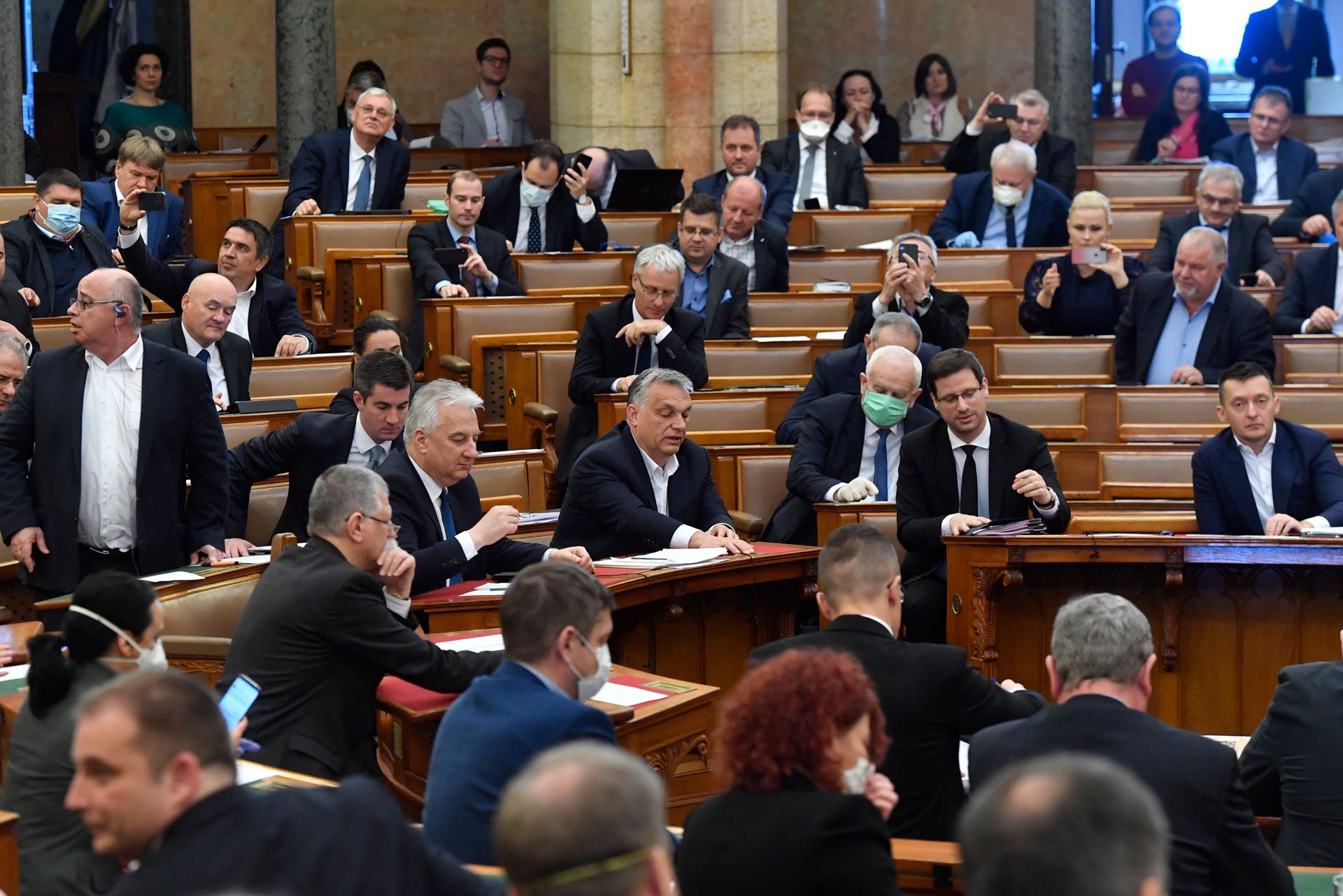 Hungarian Prime Minister Viktor Orban, center, his deputy Zsolt Semjen and other government members and MPs of the governing Fidesz party vote on a draft law concerning extraordinary measures during the plenary session of Parliament in Budapest, Hungary, 