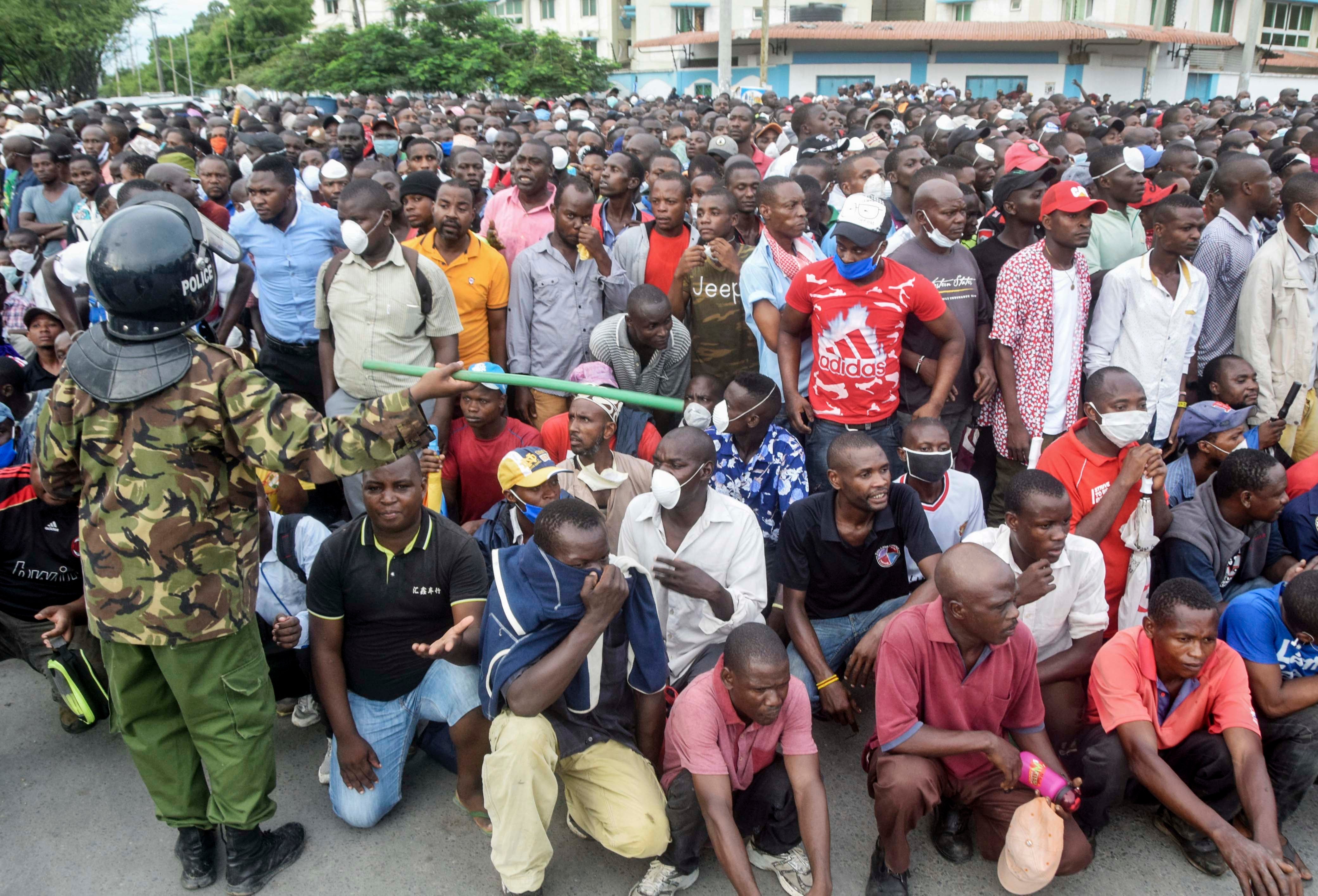 Un policier kenyan brandit un bâton devant une foule de personnes qui attendent afin de pouvoir monter à bord d’un ferry au port de Mombasa, le 27 mars 2020.