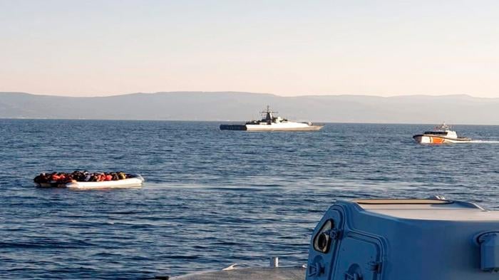 A dinghy with migrants, left, with Turkish ships in the background, in the narrow stretch of water between the eastern Greek island of Lesbos and the Turkish coast on April 2, 2021.