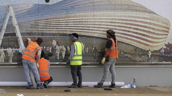 Workers in front of a mural of a stadium 
