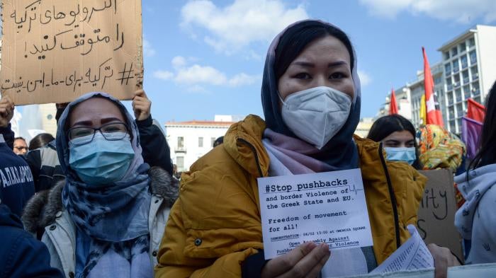 A woman at a protest holds a sign that reads "#StopPushbacks"