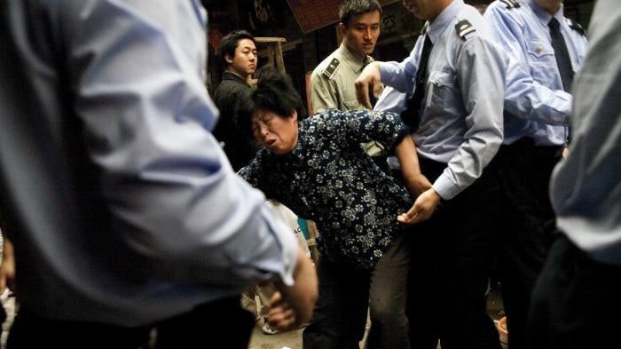 A woman fights with chengguan police as they dismantle part of her small restaurant and confiscate equipment that she stored on the sidewalk outside of her shop in the Fuzi Miao tourist market in central Nanjing, Jiangsu, China. 