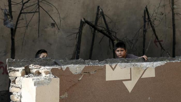Afghan boys look out from behind a damaged wall after a Taliban attack in Kabul, Afghanistan October 6, 2015.