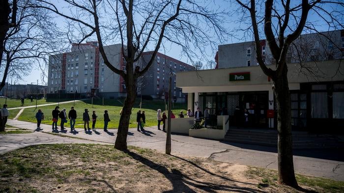 People keep their distance as they queue up in front of a post office in Pecs, Hungary, Monday, March 16, 2020.