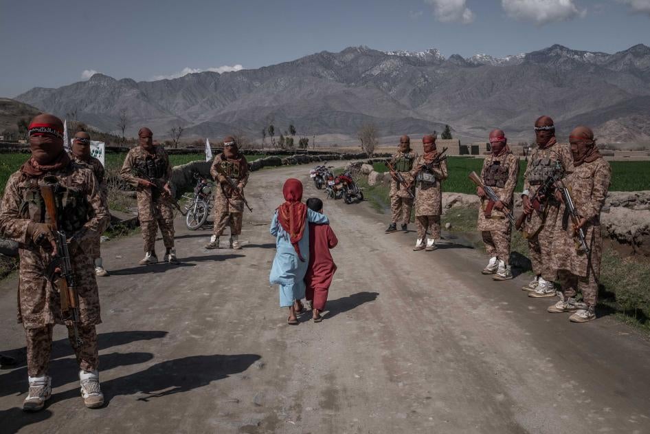 Two children walk by armed soldiers in the countryside