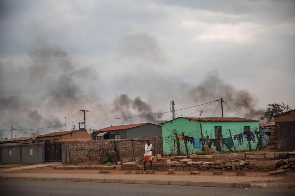 A man walks in front of a buildings, with smoke rising in the background