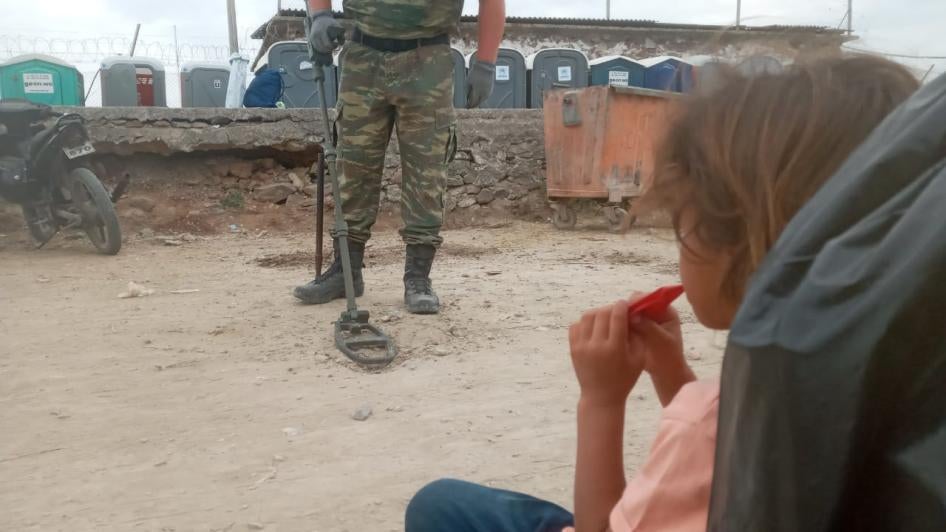 A girl from Syria living in Mavrovouni camp watches the Greek military search for unexploded munitions