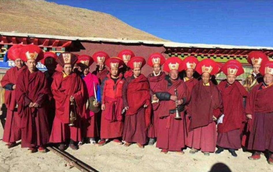 A row of monks in red outfits and headdresses pose for a photo