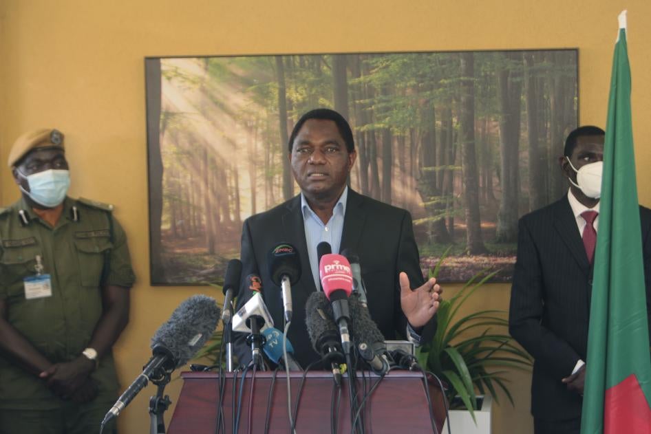 A man stands at a podium flanked by two people in face masks