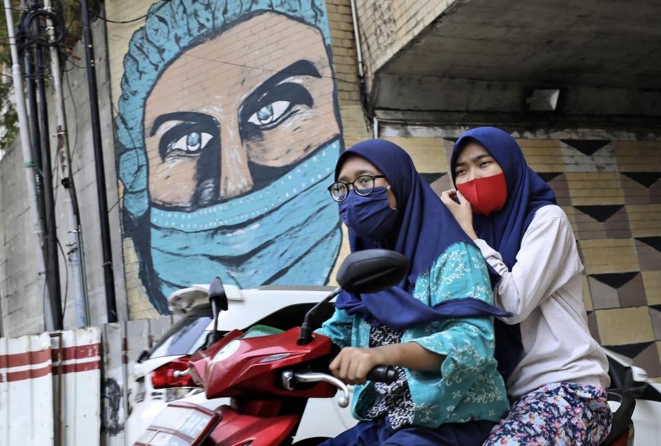 Women ride a motorbike past a large Covid-19-themed mural in Jakarta, Indonesia, October 2, 2020.
