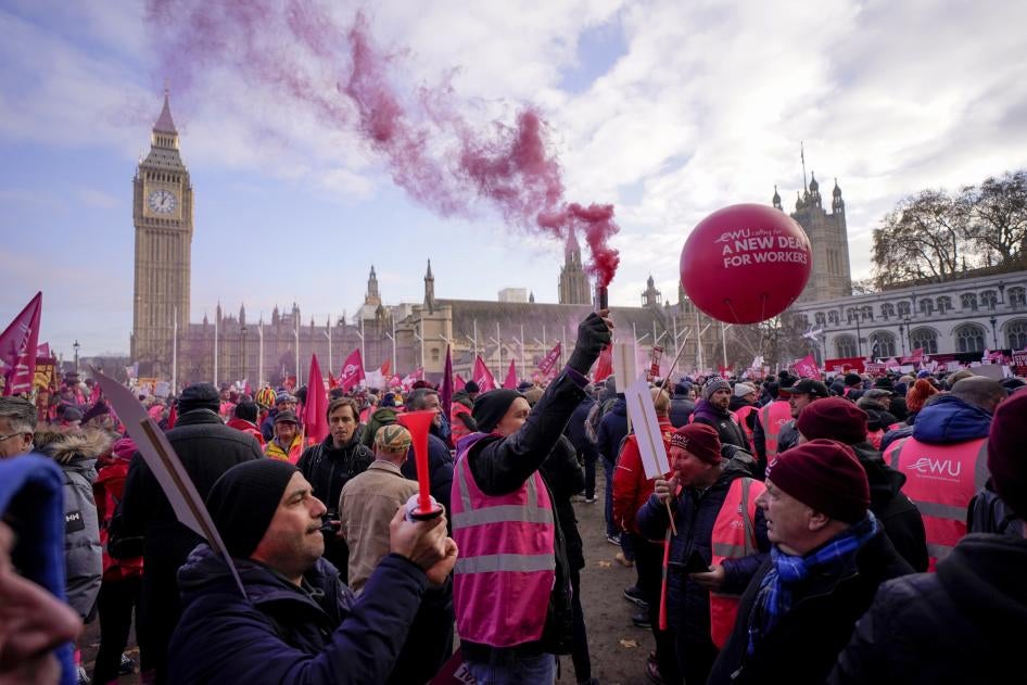 A large crowd holding signs and chanting slogans gathers in the UK