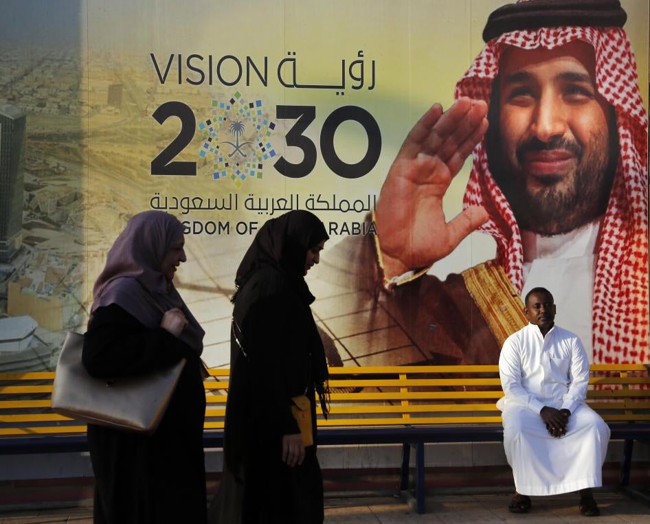 People walk past a Vision 2030 banner showing Saudi Crown Prince Mohammed bin Salman.