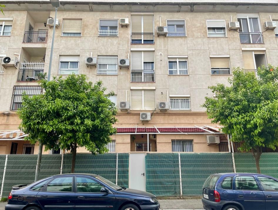 The front of a residential building in Seville (Andalusia, Spain), with outside air conditioning units and two green trees.