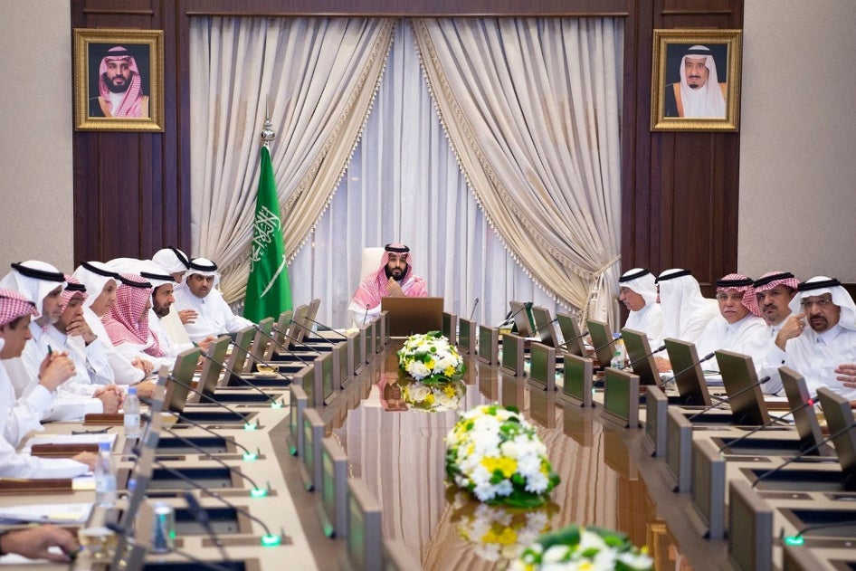 A man sits at the head of a large table during an official meeting,