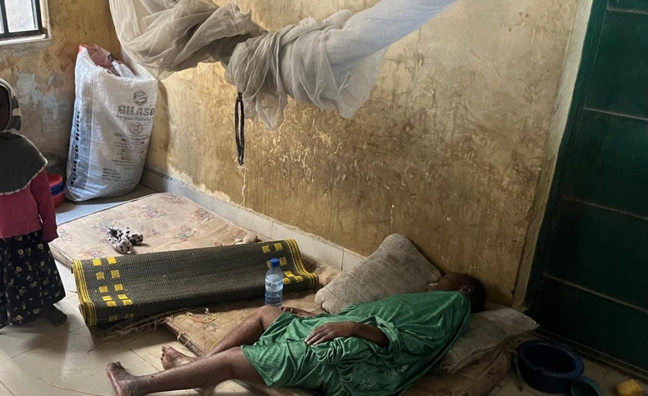 Aisha stands by her mother, lying on a worn-out and dirty mattress.