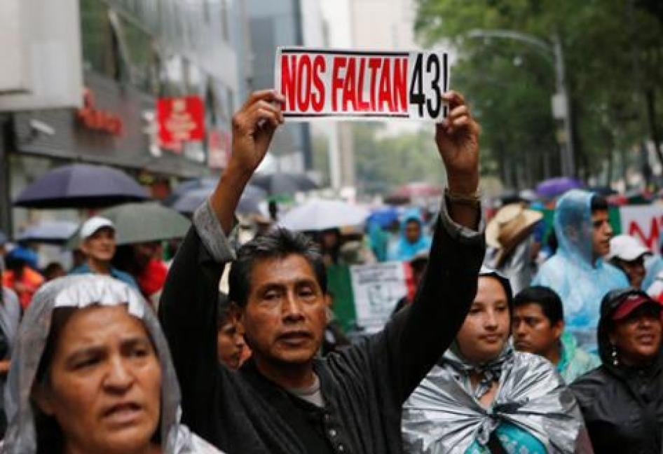 A protester holds up a sign next to relatives of some of the 43 missing students of Ayotzinapa College Raul Isidro Burgos during a march in Mexico City