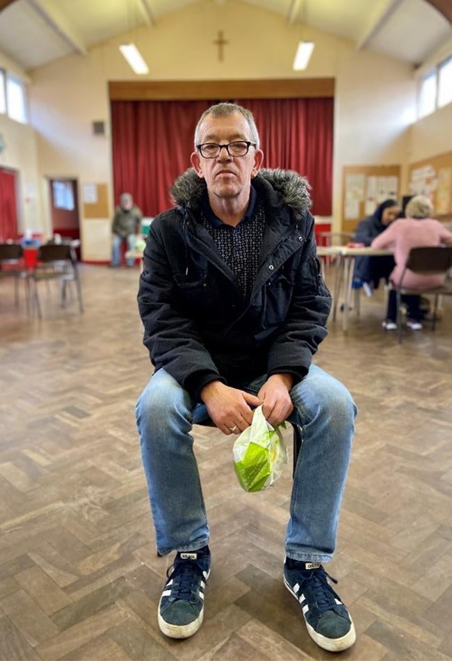 A man in a jacket and glasses sits while posing for the camera