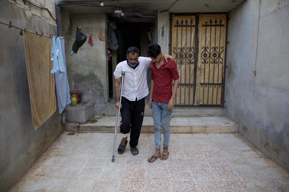 عبد الكريم بسطين (49 عاما) أصيب في الهجوم على قرية ترمانين في 6 أكتوبر/تشرين الأول، يتكئ على ابنه أمام منزلهما، سوريا، 14 أكتوبر/تشرين الأول 2023. خسر بسطيم ابن شقيقه خلال الهجوم. © 2023 علي حاج سليمان