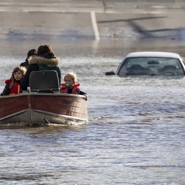 A woman and children in boat leaving behind car with floodwaters up to the roof in the background.