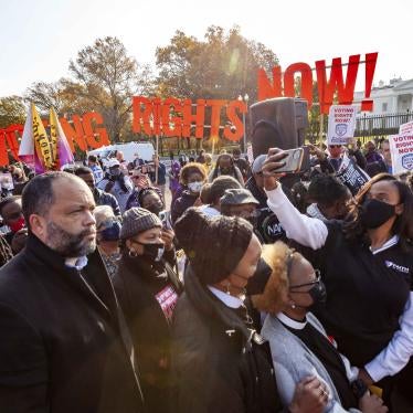 A crowd standing in front of a sign that reads "Voting Rights Now!"