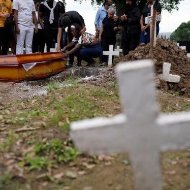 People stand and kneel next to a casket in a cemetery