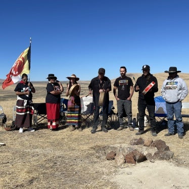 Members of People of Red Mountain and their supporters stand around a fire